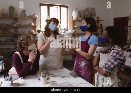 Gruppo multietnico di vasai in maschere facciali che lavorano in ceramica studio Foto Stock