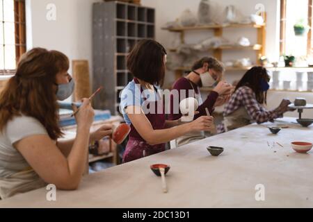 Gruppo multietnico di vasai in maschere facciali che lavorano in ceramica studio Foto Stock