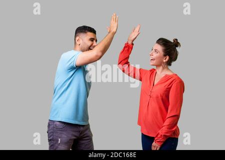 Vista laterale ritratto di entusiasti stupiti coppia giovane in abbigliamento casual in piedi dicendo ciao e dando alta cinque amici saluto ogni altro, lieto di soddisfare Foto Stock