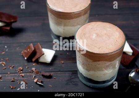 Trifles mousse tre cioccolatini in vetro su sfondo di legno scuro, fuoco selettivo. Delizioso strato fatto in casa, senza dessert al forno con bianco, latte A. Foto Stock