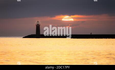 Faro al tramonto con grande sole, mare dorato e persone sul molo, Andratx, Mallorca, Spagna. Foto Stock