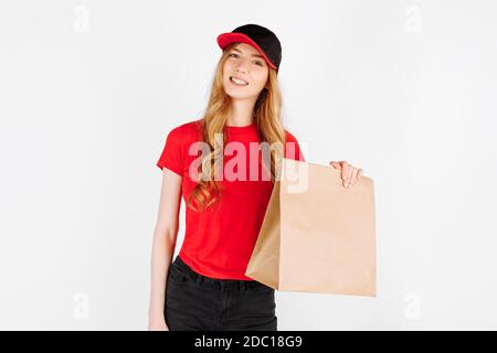 Courier-una ragazza in uniforme, tenendo un sacchetto di carta con il cibo su uno sfondo bianco. Il concetto di consegna a domicilio, ordine online Foto Stock