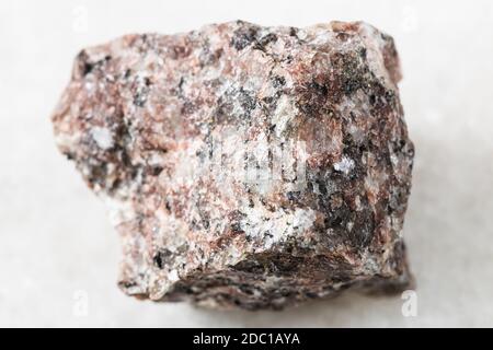 primo piano di un campione di minerale naturale proveniente dalla raccolta geologica - Ruvida roccia di granito rosa su sfondo bianco di marmo Foto Stock