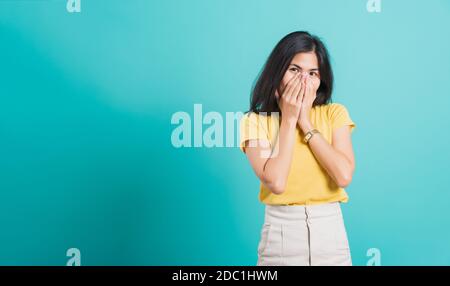 Ritratto Asiatico bella giovane donna felice indossa la t-shirt gialla lei felice eccitato ride coprendo la bocca con le mani, scatta foto in uno studio, su un blu Foto Stock