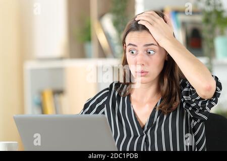 La donna stressata scopre l'errore sul portatile seduto in una scrivania a casa Foto Stock