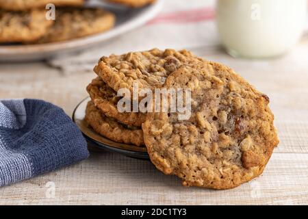Primo piano di biscotti all'uvetta di farinata d'avena su un tavolo di legno con vetro di latte e piatto di biscotti sullo sfondo Foto Stock