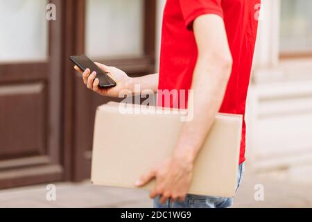 un corriere con una scatola di cartone utilizzando un telefono cellulare all'aperto Foto Stock