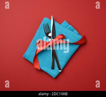 forchetta e coltello in metallo legati da un nastro di seta rossa, sfondo rosso, vista dall'alto Foto Stock
