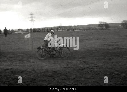 Alla fine degli anni '50, un concorrente maschile in un evento di scrambling motociclistico, che attraversa un sentiero fangoso. Inventata nel 1924, a Camberley, Surrey, in Inghilterra, le moto usate per la corsa negli anni '50 e all'inizio degli anni '60 erano poco diverse dalle moto da strada del tempo, con pochissime sospensioni. Oggi lo sport è conosciuto come motocross – il nome francese per il cross-country motociclismo – e chiamato Supercross negli Stati Uniti. Foto Stock