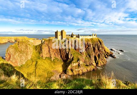 DUNNOTTAR CASTLE STONEHAVEN ABERDEENSHIRE SCOTLAND EDIFICI ILLUMINATI AL SOLE SU RIPIDE SCOGLIERE CIRCONDATO DA UN MARE PLACID Foto Stock