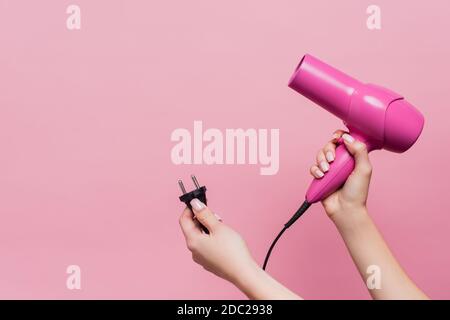 vista ritagliata del cavo di presa donna con spina e capelli essiccatore isolato su rosa Foto Stock
