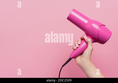 vista ritagliata della donna che tiene l'asciugacapelli isolato su rosa Foto Stock
