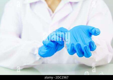 Primo piano mani biologo indossare guanti in lattice blu nitrile in camice da laboratorio indossando guanti in nitrile, facendo esperimenti in laboratorio Foto Stock