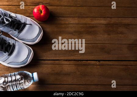 Vista dall'alto di scarpe sportive da coppia, acqua in bottiglia e mela rossa sul tavolo in legno, sneakers Grey e accessori in PALESTRA, fitness conce Foto Stock