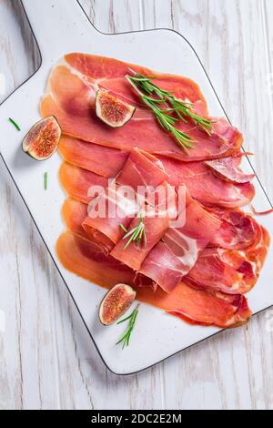 Delizioso prosciutto di Serrano con fichi freschi e rosmarino su bianco tagliere Foto Stock