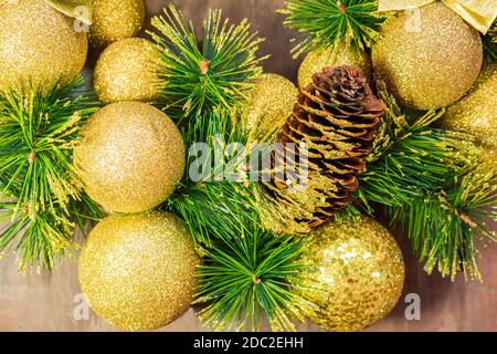Palline di Natale giallo brillante e cono con chiodi e rami di pino su sfondo di legno. Carta anno nuovo Foto Stock