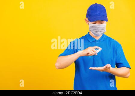 Asian giovane consegna bello uomo che indossa maschera di protezione germe virus e maschera alcool sanitizzante spray a mano, studio girato isolato su giallo b Foto Stock