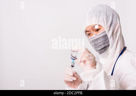 Mano di primo piano di medico o scienziato in PPE suite uniforme indossare maschera protettiva in laboratorio tenere la medicina liquido vaccino flacone e syring Foto Stock