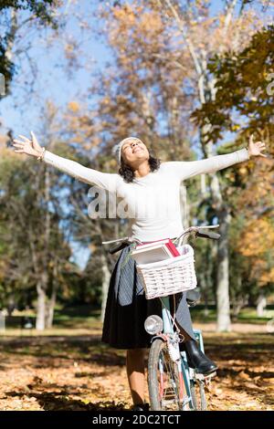 Donna brunetta che si gode una giornata autunnale nel parco. È in bicicletta. Spazio per il testo. Foto Stock