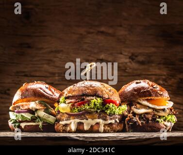 Vista frontale su tre grandi hamburger di salmone di manzo e kebab ripieni di insalata di verdure fresche e condimento Foto Stock