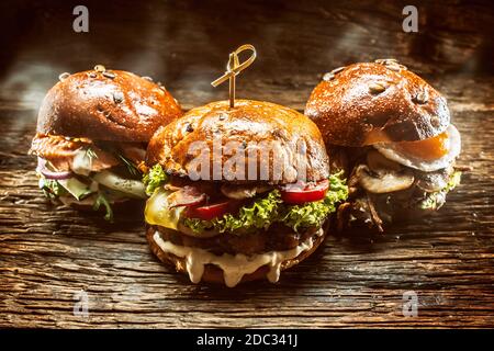Vista frontale su tre grandi hamburger di salmone di manzo e kebab ripieni di insalata di verdure fresche e condimento Foto Stock