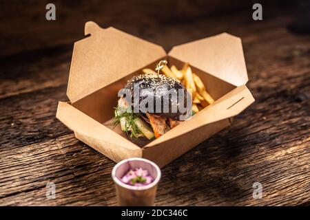 Gustoso hamburger nero da asporto in una scatola di carta riciclata su tavola di legno Foto Stock