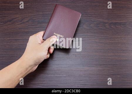 Mano dell'uomo che tiene il passaporto internazionale su un tavolo di legno scuro marrone. Foto Stock