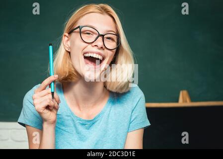 Giovane donna seduta al tavolo facendo assegnamenti biblioteca. Giovane studente felice. Giornata mondiale degli insegnanti. Felice studentessa casual con lavagna Foto Stock