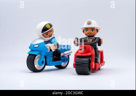 Due motociclisti in miniatura Lego isolati su sfondo grigio chiaro. Un poliziotto su una moto blu seguito da un vigile del fuoco su una moto rossa. Foto Stock