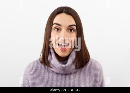 Primo piano seducente donna bruna sorridente in un pullover viola che attende con impazienza un evento emozionante, grinning esprime gioiosamente positività Foto Stock