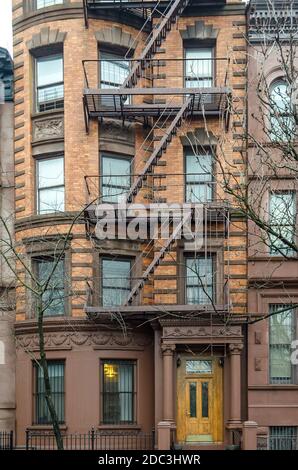 Tipico edificio di appartamenti di New York City con scale di fuga dal fuoco e porta di legno gialla all'entrata. Manhattan, New York, Stati Uniti Foto Stock