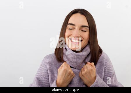 Primo piano seducente donna bruna sorridente in un pullover viola che attende con impazienza un evento emozionante, grinning esprime gioiosamente positività Foto Stock