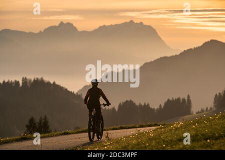 Donna attiva che cavalca la sua mountain bike elettrica al tramonto di fronte all'impressionante silhouette del Monte Saentis, Appenzell svizzera Foto Stock