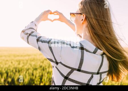 Una donna romantica cammina attraverso i campi di grano dorato e spettacoli il suo cuore con le mani Foto Stock