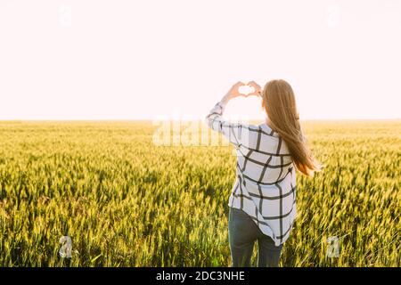 Una donna romantica cammina attraverso i campi di grano dorato e spettacoli il suo cuore con le mani Foto Stock