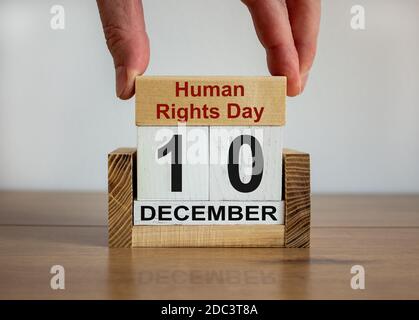 La mano maschile mette un blocco con l'iscrizione 'Human Rights Day' su cubi con la data del 10 dicembre. Bel tavolo in legno, sfondo bianco, copia spac Foto Stock