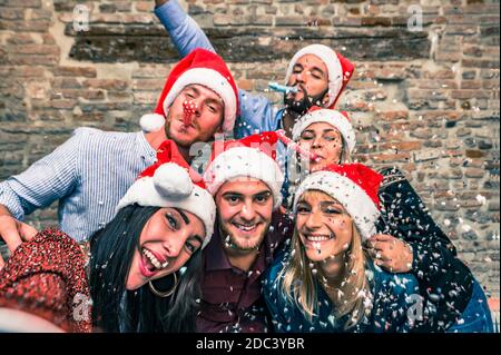 Gruppo di amici felici con la maschera viso giù in notte di cristmas gettano i confetti e soffiano nelle trombe - Gruppo di giovani colleghi celebratin Foto Stock