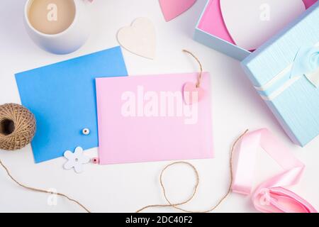 Busta rosa e blu, confezione regalo, caffè con latte e cuori su sfondo chiaro. Foto Stock