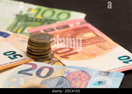 Banconote in euro e monete impilate su sfondo scuro Foto Stock