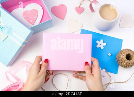 Le mani di una donna tengono una busta rosa su uno sfondo romantico in colori rosa e blu. Foto Stock