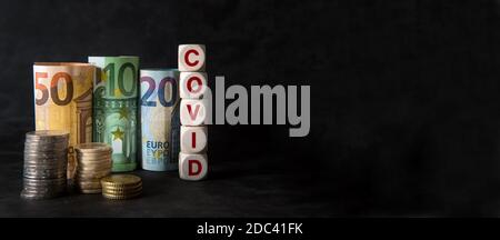 banconote in euro arrotolate e monete impilate con l'iscrizione COVID su sfondo nero e spazio di copia Foto Stock