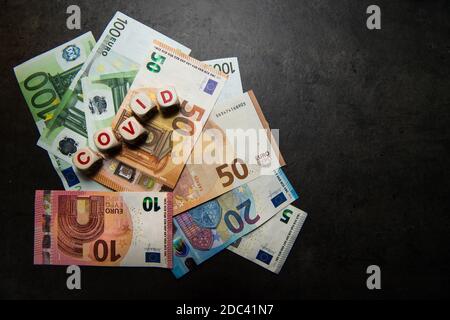 banconote in euro su sfondo scuro con scritta covid vista dall'alto Foto Stock