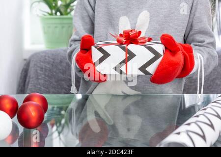 Una ragazza in un maglione grigio con un coniglio tiene un regalo di Natale con i mittenti rossi nelle sue mani. Capodanno, Natale, vacanze invernali, palle di Natale, regalo Foto Stock