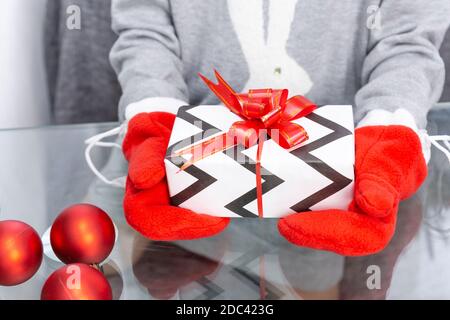 Una ragazza in un maglione grigio con un coniglio tiene un regalo di Natale con i mittenti rossi nelle sue mani. Capodanno, Natale, vacanze invernali, palle di Natale, regalo Foto Stock