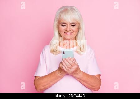 Ritratto fotografico di simpatica nonna utilizzando smartphone navigazione internet sorridente isolato su sfondo di colore rosa pastello Foto Stock