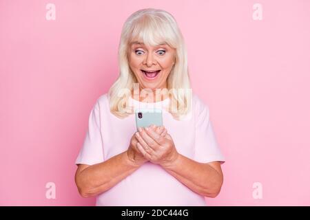 Ritratto fotografico di stupito messaggio di testo granny sorpreso utilizzando il cellulare con bocca aperta isolata su sfondo di colore rosa pastello Foto Stock