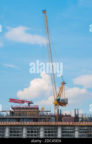 Spostamento della gru a torre gialla e costruzione di edifici incompiuta contro il blu cielo Foto Stock