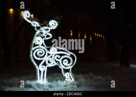 Figura di cervo offuscato da una ghirlanda incandescente nella notte oscura d'inverno nella neve. Sfondo delle vacanze di Natale Foto Stock