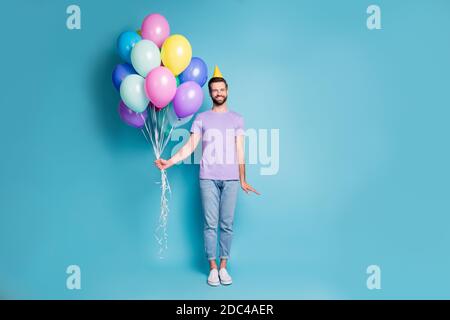 Foto di dimensioni del corpo a lunghezza intera di divertente compleanno uomo con palloncini con cono giallo sorridente isolati di colore blu brillante sfondo Foto Stock