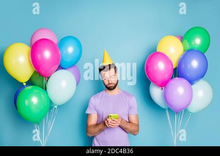 Ritratto fotografico di ragazzo annoiato che scrive sms perché nessuno è venuto a festa di compleanno che tiene il telefono in due mani isolato su sfondo di colore blu pastello Foto Stock